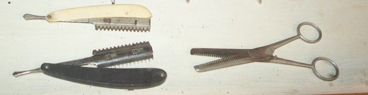 Two folding razors with comb guards and a pair of thinning shears laid out on a pale bench