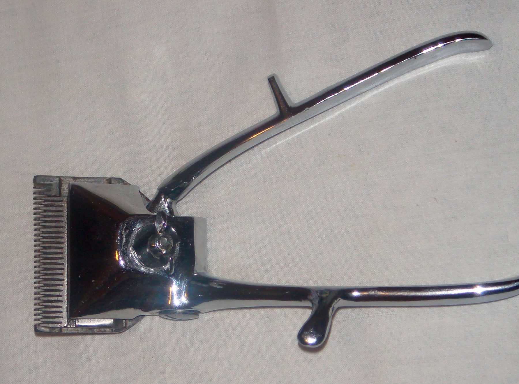 A hand-operated barber clipper lying on pale cloth, blade and lever in profile