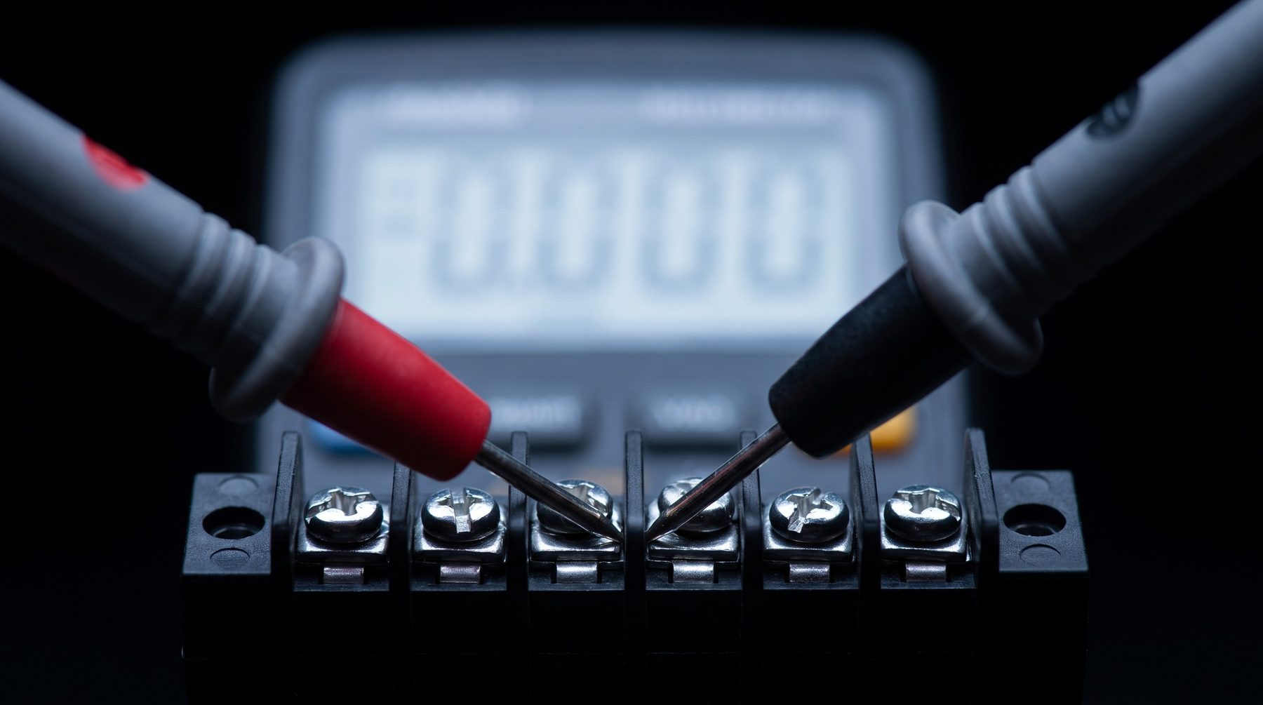 Multimeter probes on a terminal block, display digits out of focus
