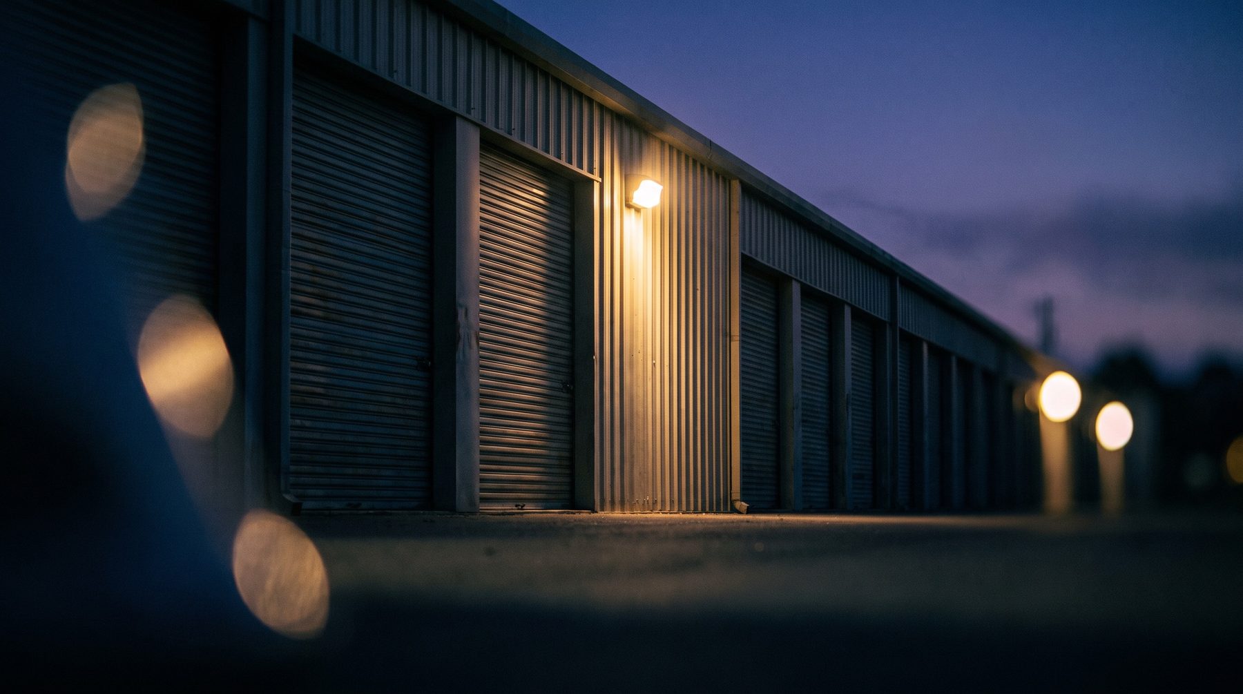 Self storage facility exterior at dusk, rows of unit doors with a security light on